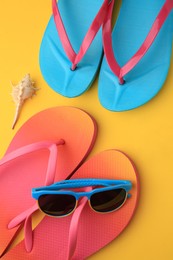 Photo of Flip flops and sunglasses on yellow background, flat lay. Beach accessories