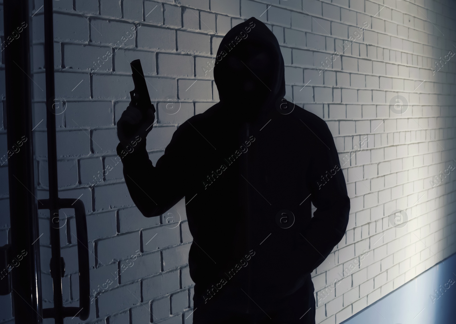 Photo of Silhouette of man with gun in hoodie indoors. Dangerous criminal