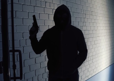 Silhouette of man with gun in hoodie indoors. Dangerous criminal