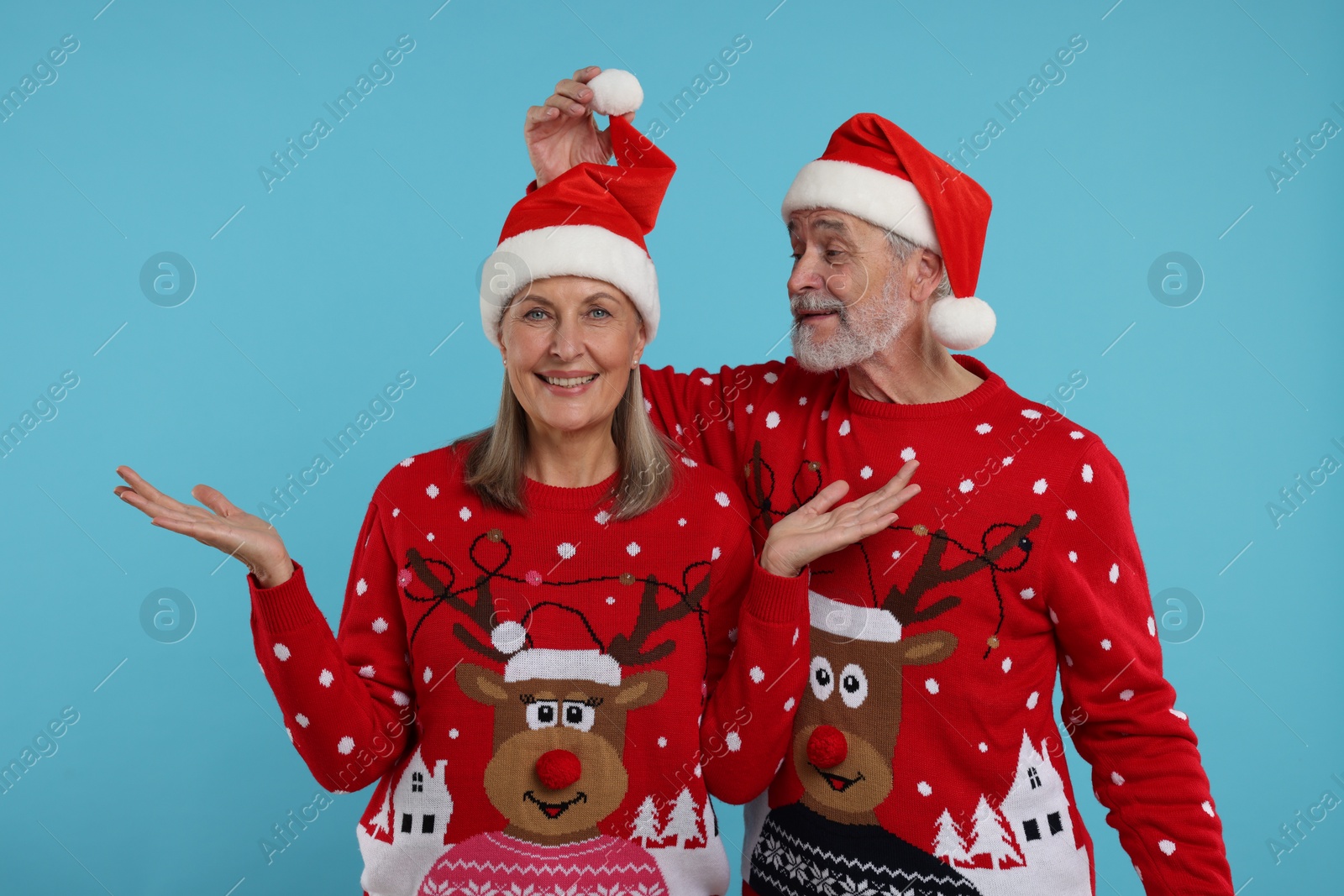 Photo of Happy senior couple in Christmas sweaters and Santa hats on light blue background