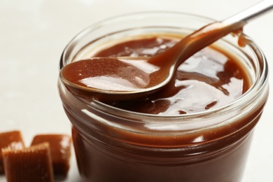 Jar with tasty caramel sauce and spoon on table, closeup