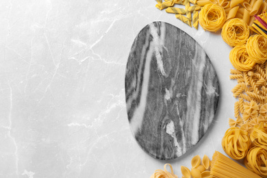 Photo of Different types of pasta and empty board on light grey marble table, flat lay. Space for text