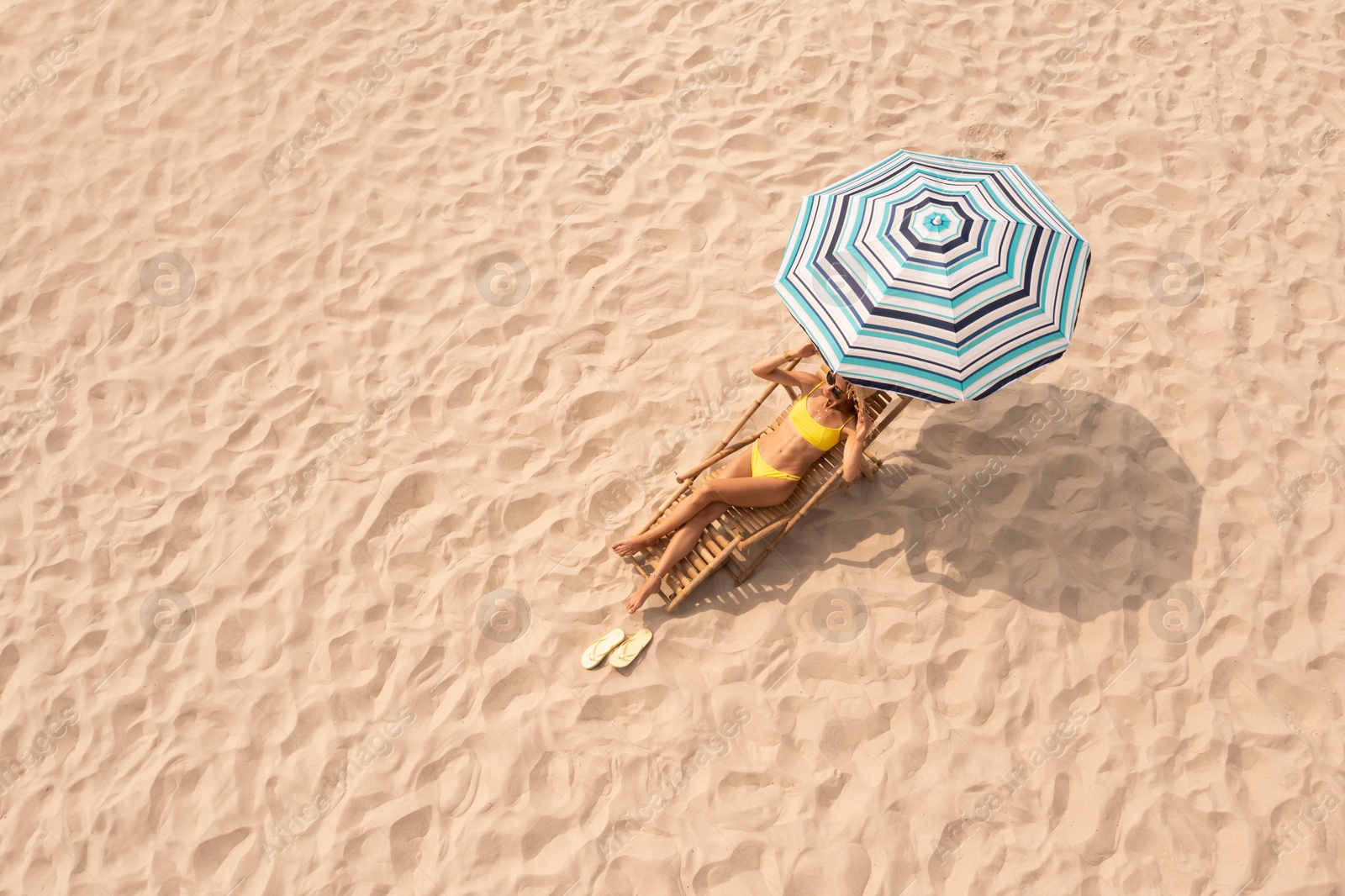 Image of Woman resting in sunbed under striped beach umbrella at sandy coast, space for text