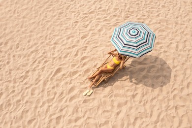 Woman resting in sunbed under striped beach umbrella at sandy coast, space for text