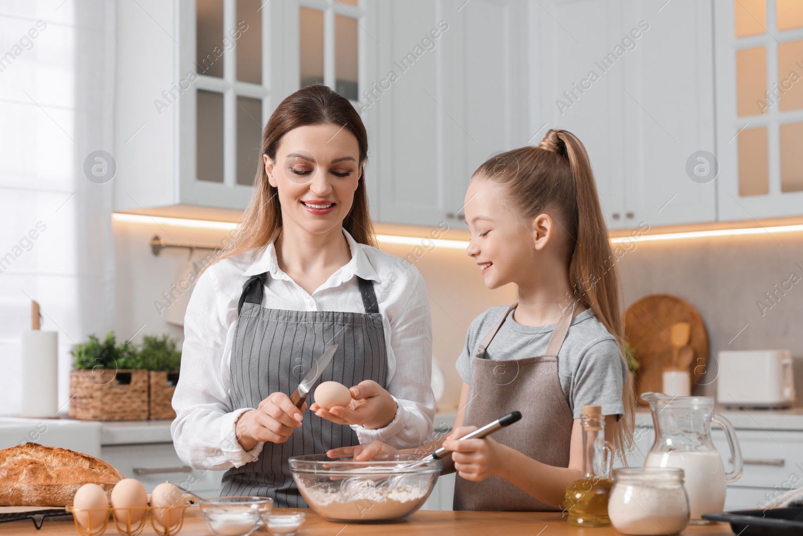Photo of Making bread. Mother and her daughter preparing dough at wooden table in kitchen