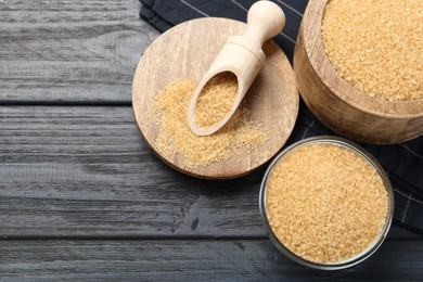 Photo of Brown sugar in bowls and scoop on black wooden table, flat lay. Space for text
