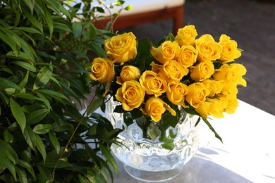 Photo of Beautiful bouquet of yellow roses in glass vase on white table outdoors