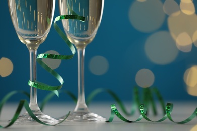 Photo of Glasses of champagne and serpentine streamer on table against blurred lights, closeup. Space for text