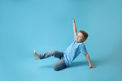 Photo of Happy little boy dancing on light blue background