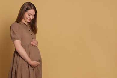 Photo of Happy young pregnant woman on light brown background. Space for text
