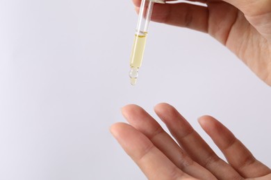 Photo of Woman applying cosmetic serum onto her finger on white background, closeup. Space for text