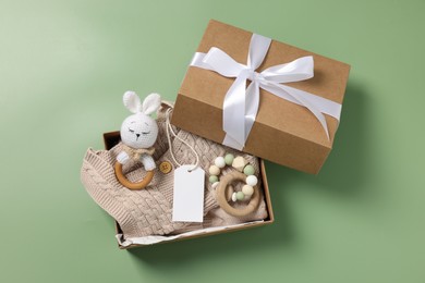 Photo of Different baby accessories, knitted sweater and blank card in box on green background, top view