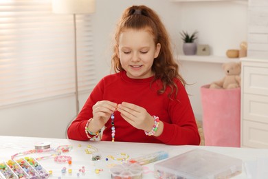 Photo of Cute girl making beaded jewelry at table in room