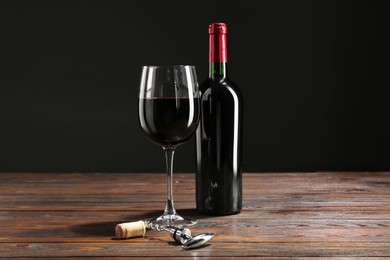 Photo of Corkscrew, glass and bottle of red wine on wooden table against black background