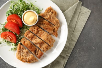 Photo of Tasty cut schnitzel served with sauce, microgreens and tomato on grey textured table, top view. Space for text