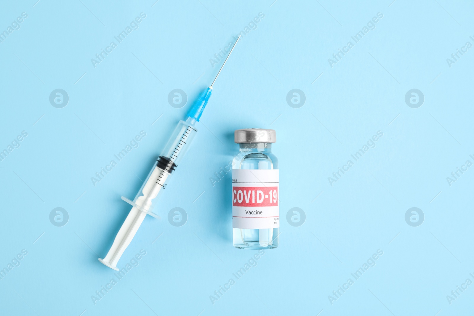 Photo of Vial with coronavirus vaccine and syringe on light blue background, flat lay