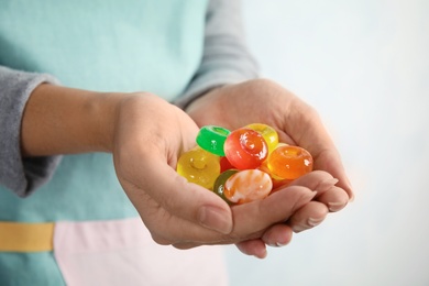 Photo of Woman holding many colorful candies on light background, closeup