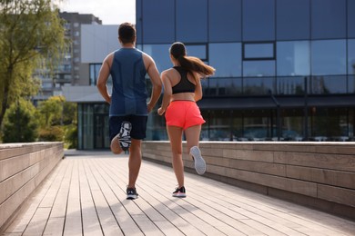 Photo of Healthy lifestyle. Couple running outdoors on sunny day, back view. Space for text