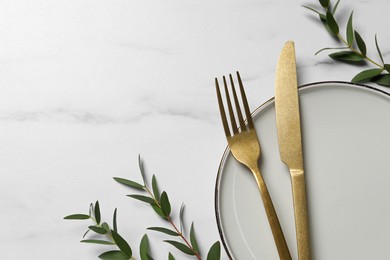 Photo of Stylish setting with cutlery and eucalyptus leaves on white marble table, flat lay. Space for text