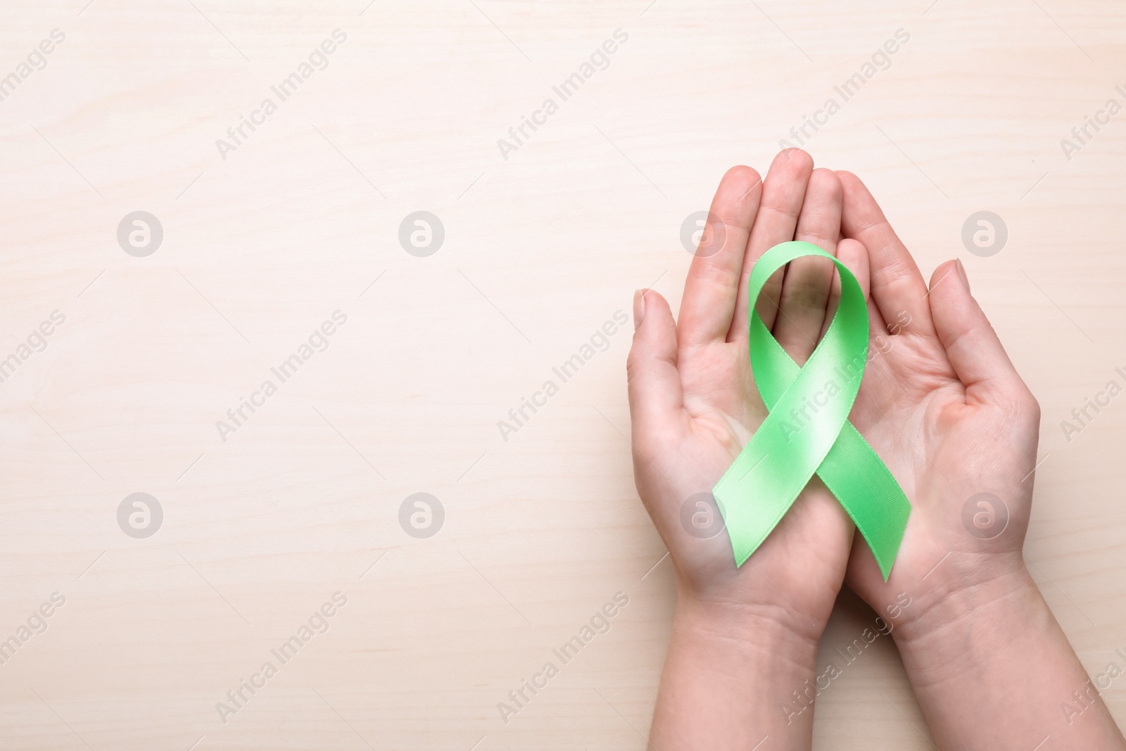 Photo of World Mental Health Day. Woman holding green ribbon on wooden background, top view with space for text