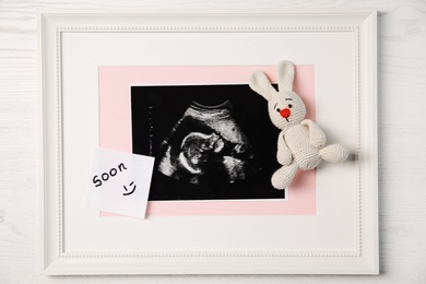 Photo of Ultrasound photo of baby and toy on wooden background, top view