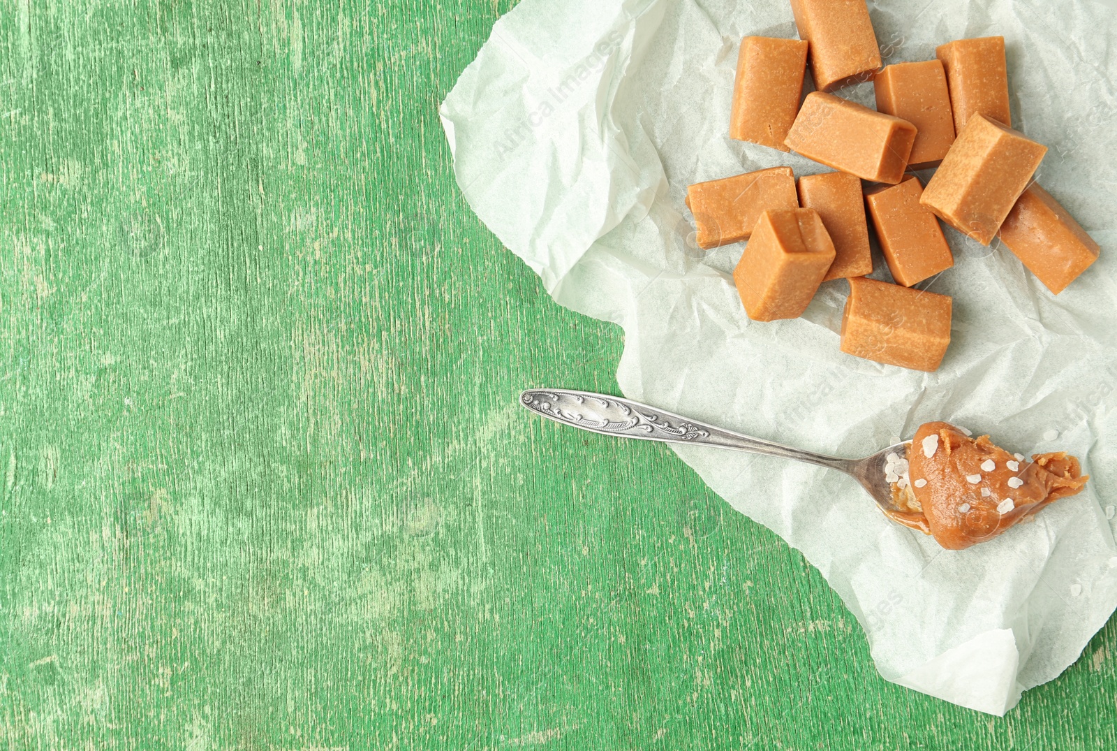 Photo of Delicious candies and salted caramel sauce in spoon on wooden table, top view