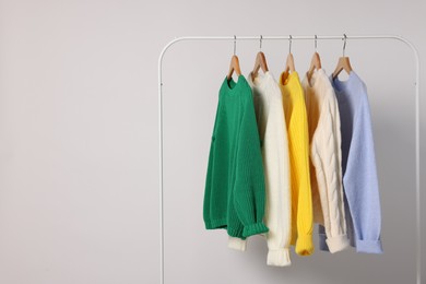 Photo of Rack with different warm sweaters on light background. Space for text