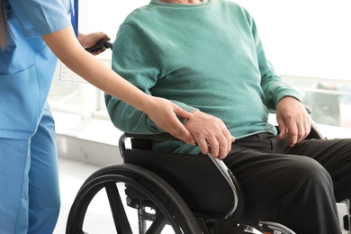 Photo of Nurse assisting senior man in wheelchair at hospital, closeup