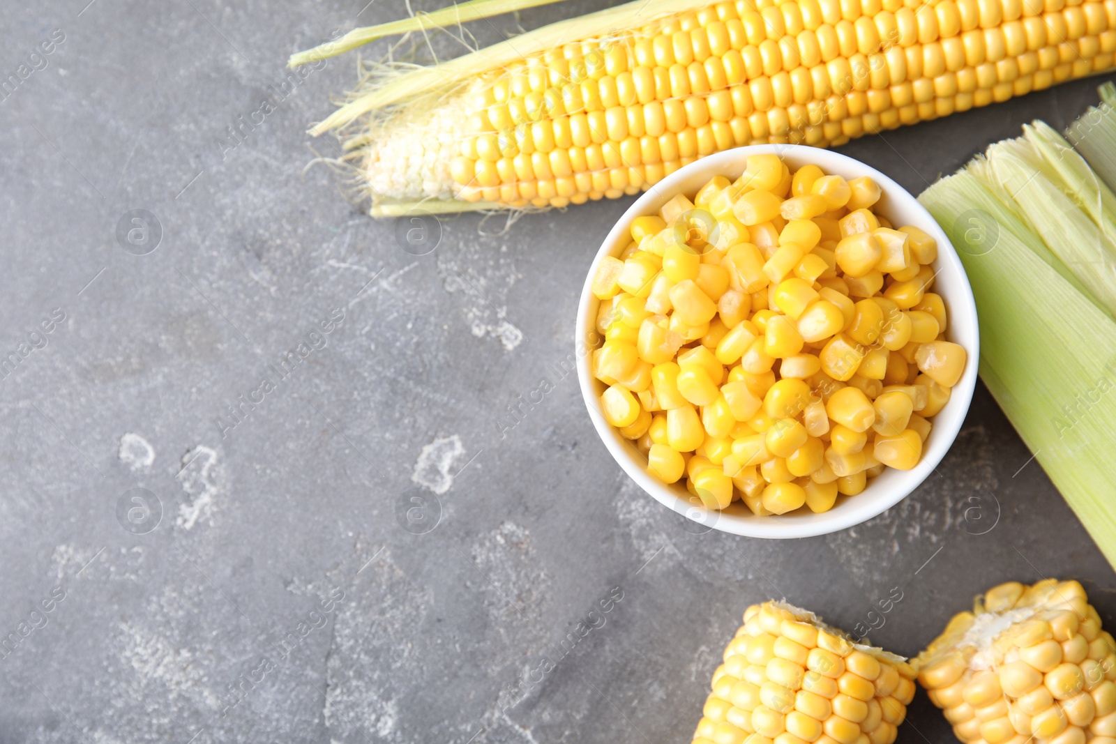 Photo of Bowl with corn kernels and ripe cobs on grey background, top view. Space for text