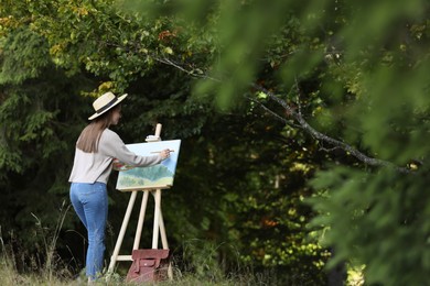 Photo of Young woman drawing on easel in forest