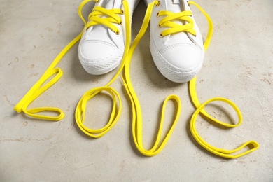 Photo of Pair of stylish shoes and word Love made with yellow laces on grey background