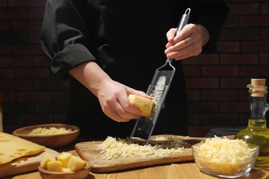 Photo of Woman grating cheese at wooden table, closeup