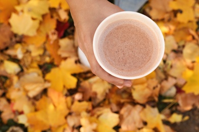 Photo of Woman holding cup of hot drink in park with fallen leaves, above view. Autumn season