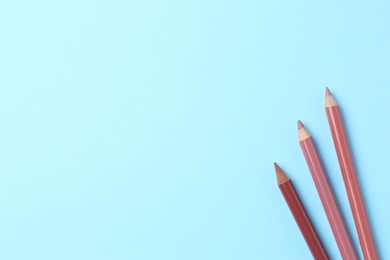 Photo of Different lip pencils on light blue background, flat lay with space for text. Cosmetic product