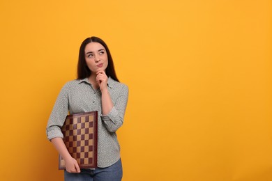 Photo of Thoughtful woman with chessboard on orange background, space for text