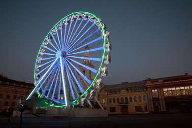 Photo of Big glowing Ferris wheel on city street at night, low angle view
