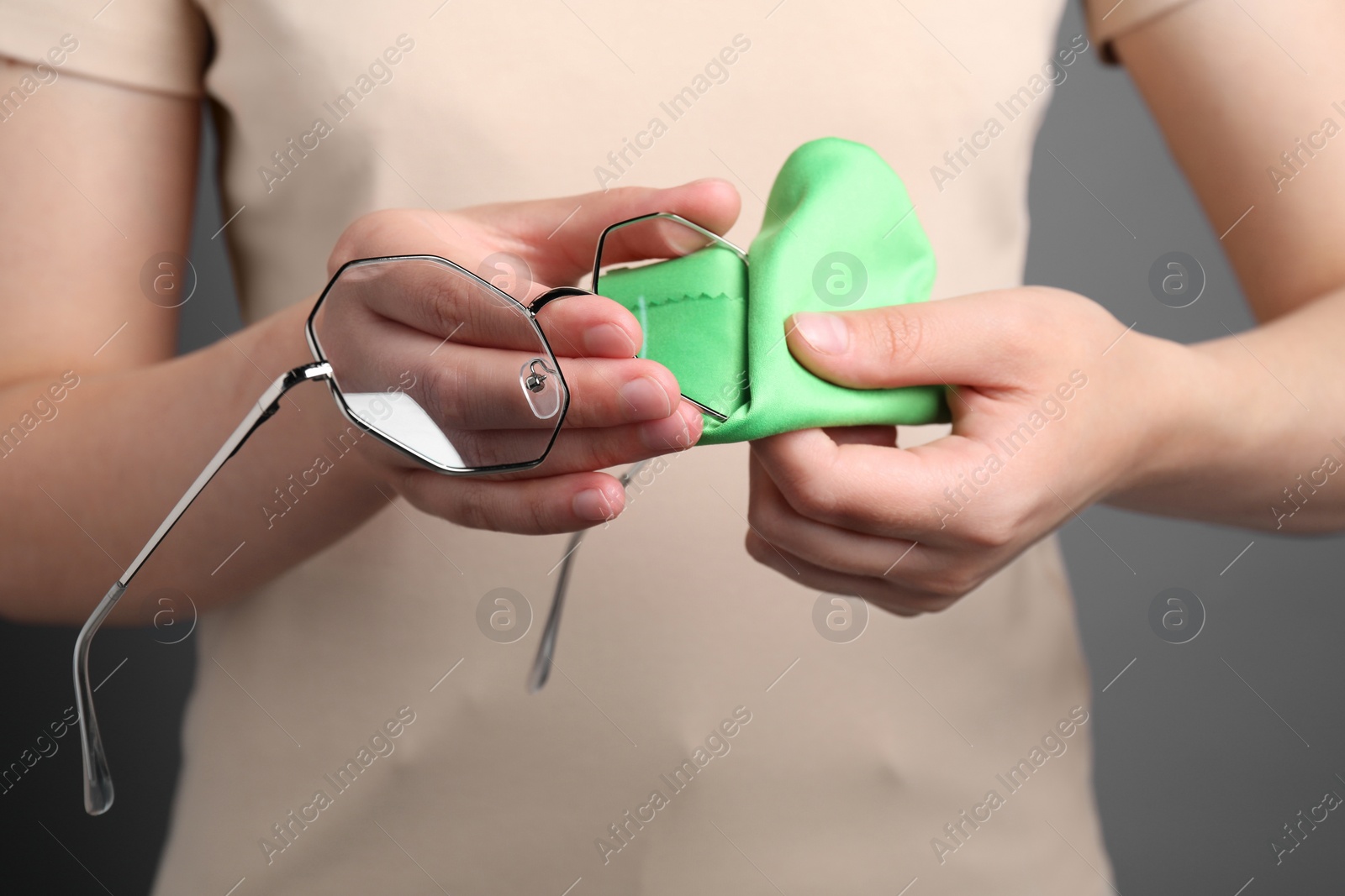 Photo of Woman wiping her glasses with microfiber cloth on grey background, closeup