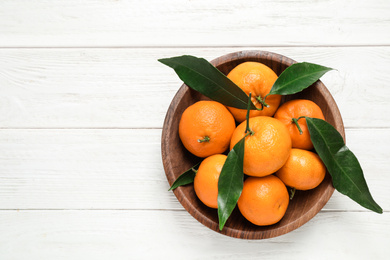 Photo of Fresh ripe tangerines with leaves and space for text on white wooden table, top view. Citrus fruit