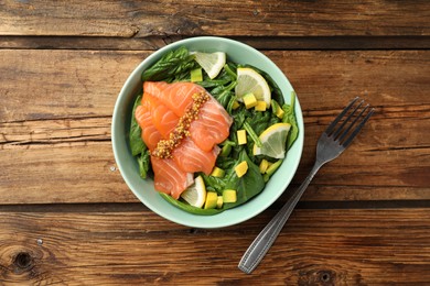 Photo of Delicious salmon with spinach, lemon and avocado served on wooden table, flat lay