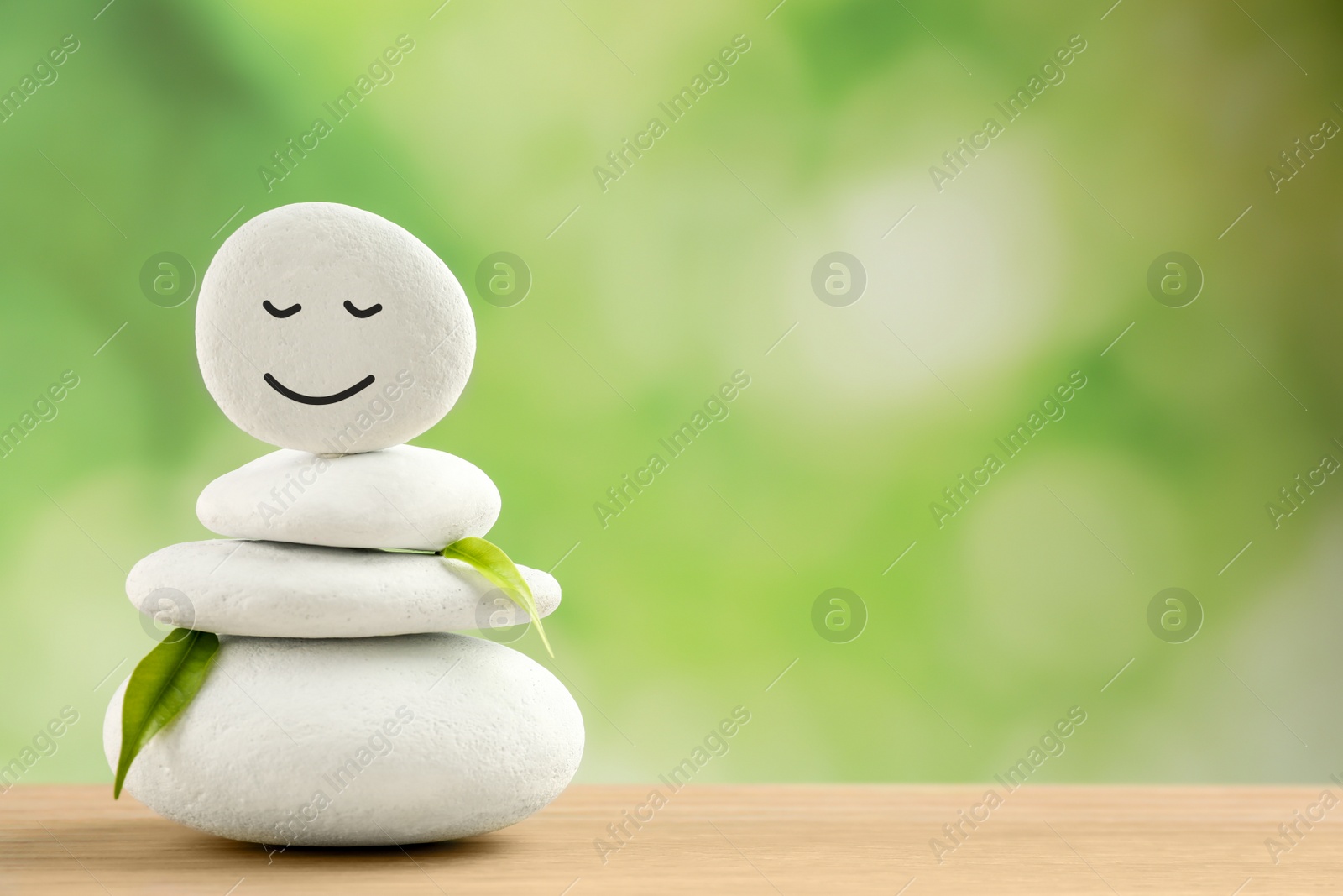 Photo of Stack of stones with drawn happy face and leaves on wooden table, space for text. Zen concept