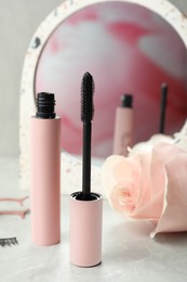 Photo of Mascara for eyelashes and flower on light table. Makeup product