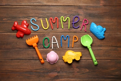 Photo of Text SUMMER CAMP made of modelling clay and different sand molds on wooden table, flat lay