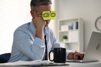 Photo of Man with fake eyes painted on sticky notes snoozing at workplace in office