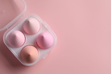 Photo of Makeup sponges in plastic container on pink background, top view. Space for text