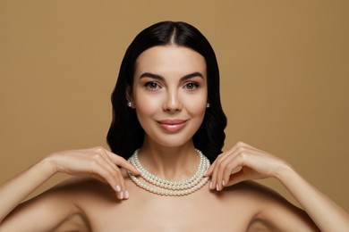 Photo of Young woman wearing elegant pearl jewelry on brown background