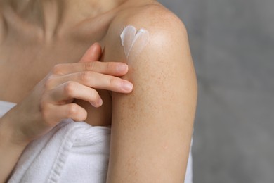 Photo of Woman applying body cream onto shoulder near grey wall, closeup