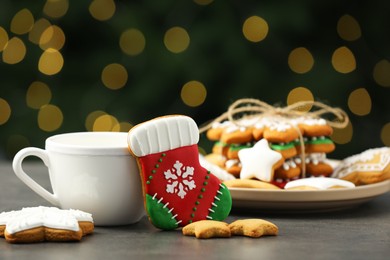 Photo of Decorated cookies and hot drink on grey table against blurred Christmas lights