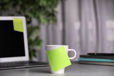 Photo of Cup with blank sticky note on white wooden table indoors. Space for text