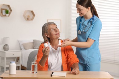 Photo of Young healthcare worker consulting senior woman at wooden table indoors