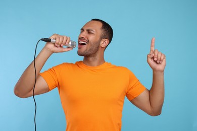 Photo of Handsome man with microphone singing on light blue background